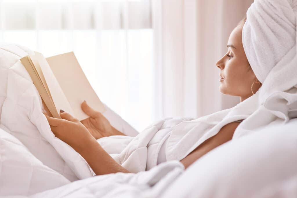 Beautiful young woman reading a book in bed